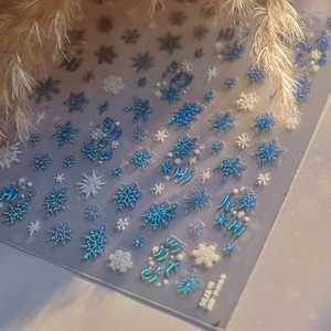 Dettaglio di adesivi per unghie con fiocchi di neve olografici blu e bianchi invernali