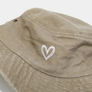 Detail of khaki cotton bucket hat showing fine heart embroidery and metal ventilation eyelet