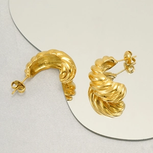 Détail de créoles dorées côtelées sur un miroir avec reflet pour montrer la texture