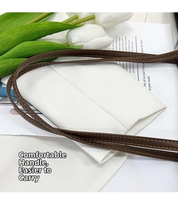 Détail des poignées en cuir marron avec coutures précises sur un sac fourre-tout en toile