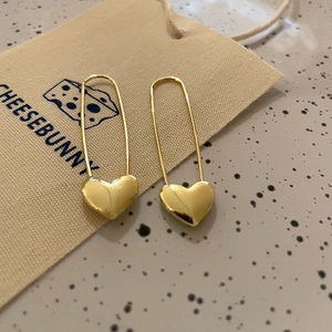 Chic gold heart safety pin earrings displayed on a soft jewelry pouch for elegant styling