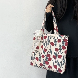 Detail of beige canvas tote bag with red poppy floral print and lace charm accessory