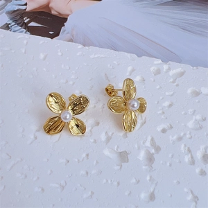Macro detail of gold flower earrings with brushed texture and center pearls on stone