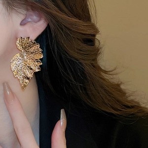 Detailed view of oversized golden leaf earrings with intricate textured vein patterns