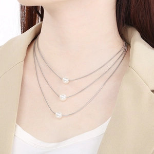 Detailed close-up of a three-layer silver snake chain necklace with round white pearls