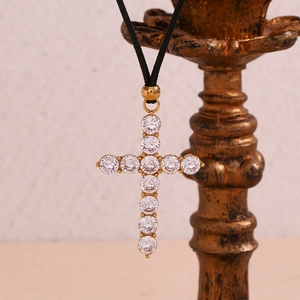 Macro detail of 18K gold plated cross pendant with cubic zirconia on black cord