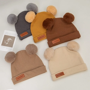 Close-up of five colorful baby winter hats featuring faux cashmere and dual pom-poms