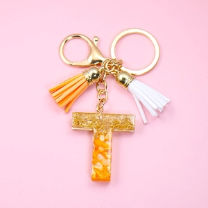 Detail of letter T resin keychain with gold foil flakes and orange tassel charms