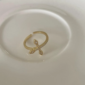 Detail of a golden cross ring with pavé-set zircons resting on a white ceramic plate