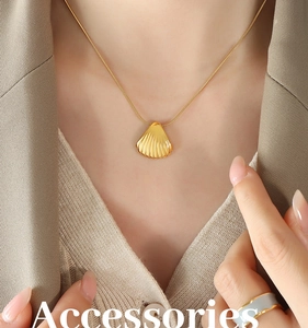 Close-up of a gold shell pendant on a snake bone chain worn over a beige knit sweater