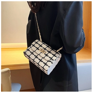 Detail view of black and white tweed crossbody bag with gold chain strap on shoulder
