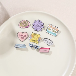 Detailed set of nine colorful enamel daisy and heart alloy brooches on a ceramic tray