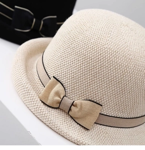 Dettaglio di un cappello da sole intrecciato con fiocco e bordo nero su fondo bianco