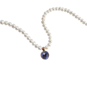 Detail of round white pearl necklace featuring a blue gemstone pendant in rose gold