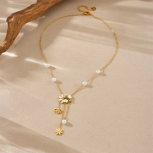 Collana dorata con ciondolo ape e margherita con perle su sfondo sabbia naturale