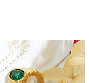 Vue détaillée d'une bague dorée ornée d'une pierre verte sur un pochon en tissu