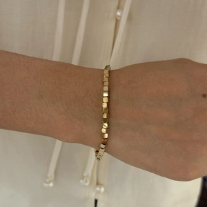 Detail of a minimalist gold cube-shaped stainless steel bracelet worn on the wrist