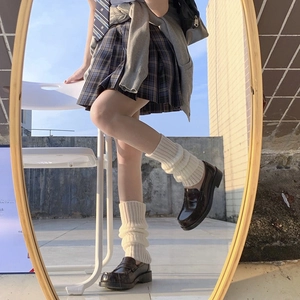 Close-up of white knitted leg warmers paired with plaid skirt and brown leather shoes