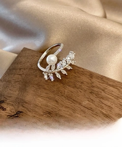 Macro di un anello a foglia argentato con perla e zirconi su sfondo di seta