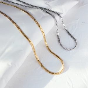 Detailed view of flat snake bone chain necklaces in gold and silver finish on white stone