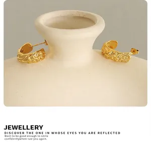 Detail of gold C-shape earrings with lava texture hanging on a ceramic vase