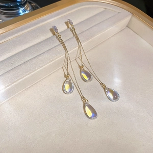 Detail view of gold drop tassel earrings with iridescent crystal charms on beige tray