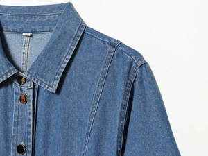 Detailaufnahme des blauen Denim-Hemdkragens mit Metallknöpfen und Kontrastnähten