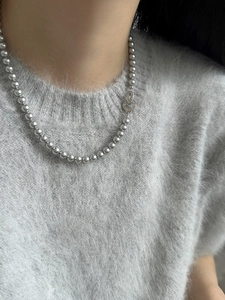 Close-up of minimalist silver pearl necklace on gray sweater with unique clasp detail