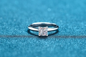 Macro shot of princess cut moissanite ring with silver four-claw setting on blue background