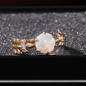 Macro di anello a foglia dorato con opale rotondo e diamanti lucidi su scatola nera