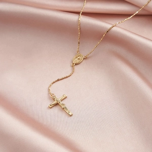 Close-up of golden cross necklace with oval holy medal on soft pink satin background