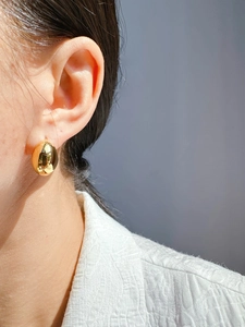 Detail shot of a polished gold oval hoop earring worn by a model in soft natural light