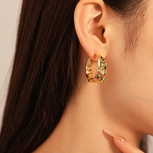Close-up of golden irregular twisted C-shape metal hoop earrings on female model