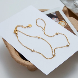 Detail of a gold-plated link bracelet with five white zircons on a white card