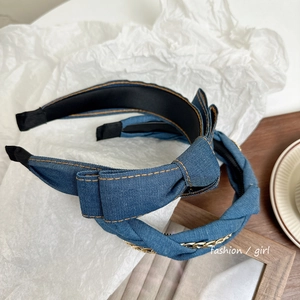Detail of blue denim headband featuring bow design and woven metal chain accent