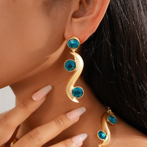 Close-up of vintage gold wavy earrings with three round blue stones on a model's ear