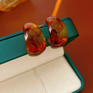 Detailed macro shot of amber C-shaped earrings on a textured dark green jewelry box