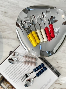 Close-up of stainless steel cutlery with colorful beaded ceramic handles on a silver tray