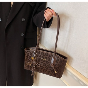 Détail du cabas léopard avec breloque tissée et logo doré sur cuir marron foncé élégant