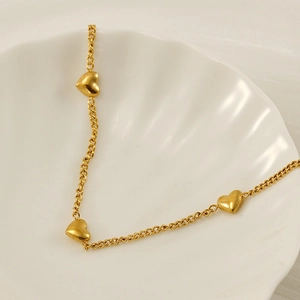 Collier gourmette doré élégant avec trois pendentifs coeur sur une assiette coquillage
