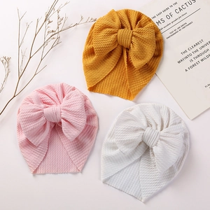 Detail of baby turban hats with large bows in pink, yellow, and white waffle knit fabric