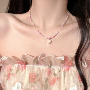 Détail du collier de perles roses avec pendentif cœur porté par un mannequin en été