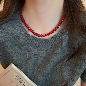 Close-up of deep red glass beaded necklace worn by a model on grey knitwear