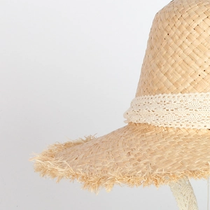 Detail of raffia straw hat edge featuring white lace ribbon and frayed fringe texture