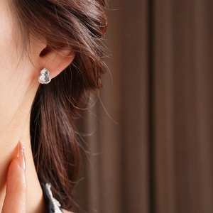 Close-up of a silver gourd shaped stud earring worn by a model in a soft lighting setting