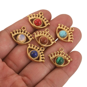 Golden evil eye pendants with natural colorful stones held in hand for scale