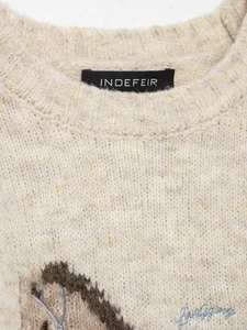Detailed close-up of brand label and blue embroidery on beige knit wool sweater