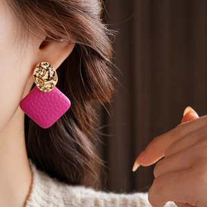 Macro view of gold irregular metal studs with magenta leather square pendants on model