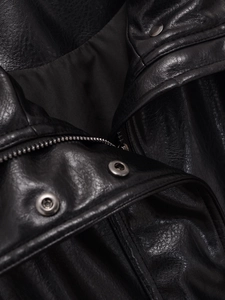 Detailed macro view of the black faux leather jacket neckline and silver metal button