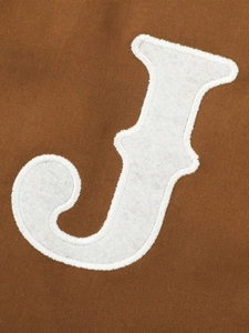 Macro detail van wit vilt letter J borduurwerk op bruine canvas stof van de jas